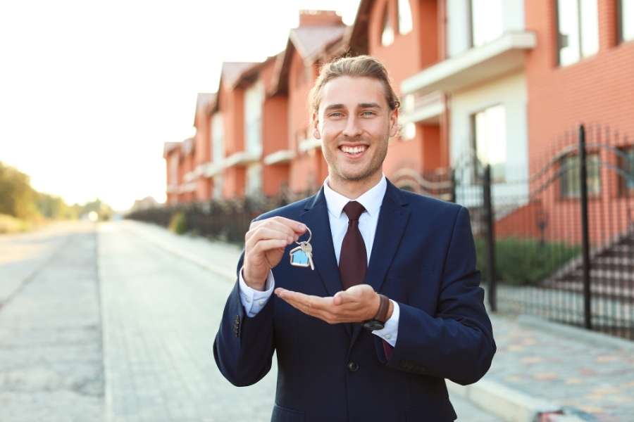 Un agent immobilier sourit en présentant les clés d'un programme immobilier neuf.
