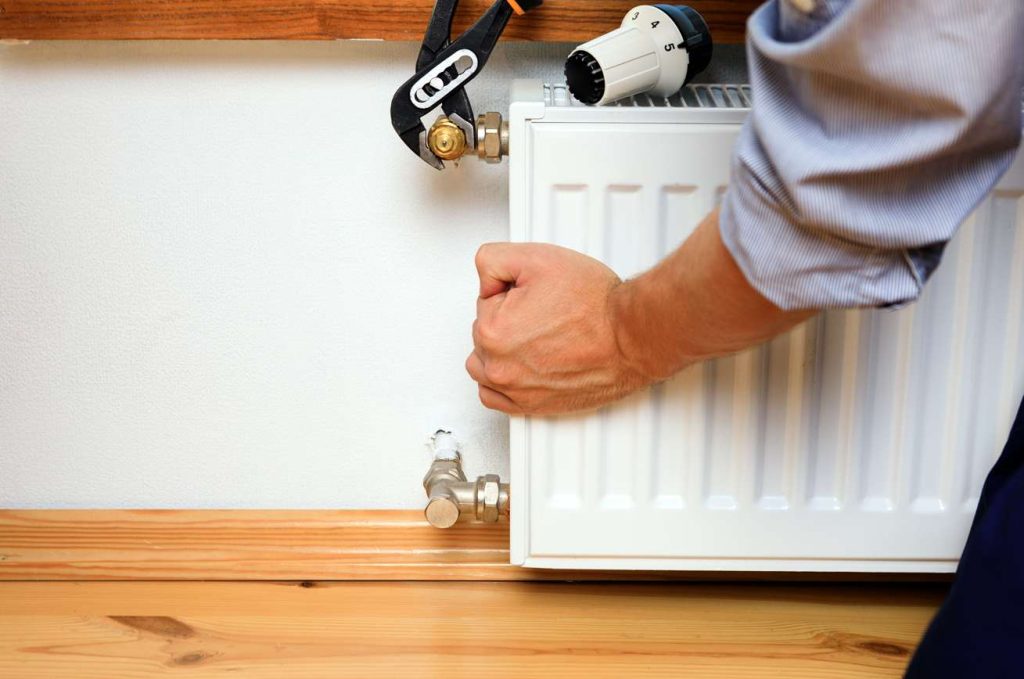 Une personne répare un radiateur pour résoudre une panne chauffage central cause et solution