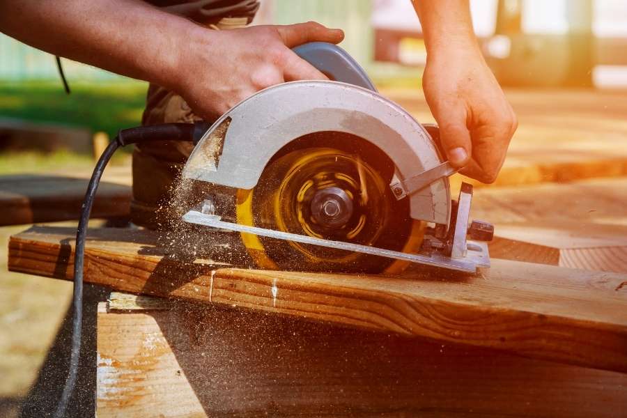 Un artisan utilise une première scie circulaire pour couper une planche en bois en dégageant de la sciure.
