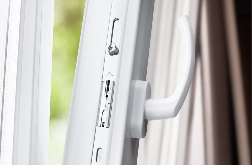 Gros plan sur la crémone et la poignée d'une fenêtre oscillo-battante blanche, montrant le mécanisme interne d'une serrure multipoint pour menuiserie pvc.